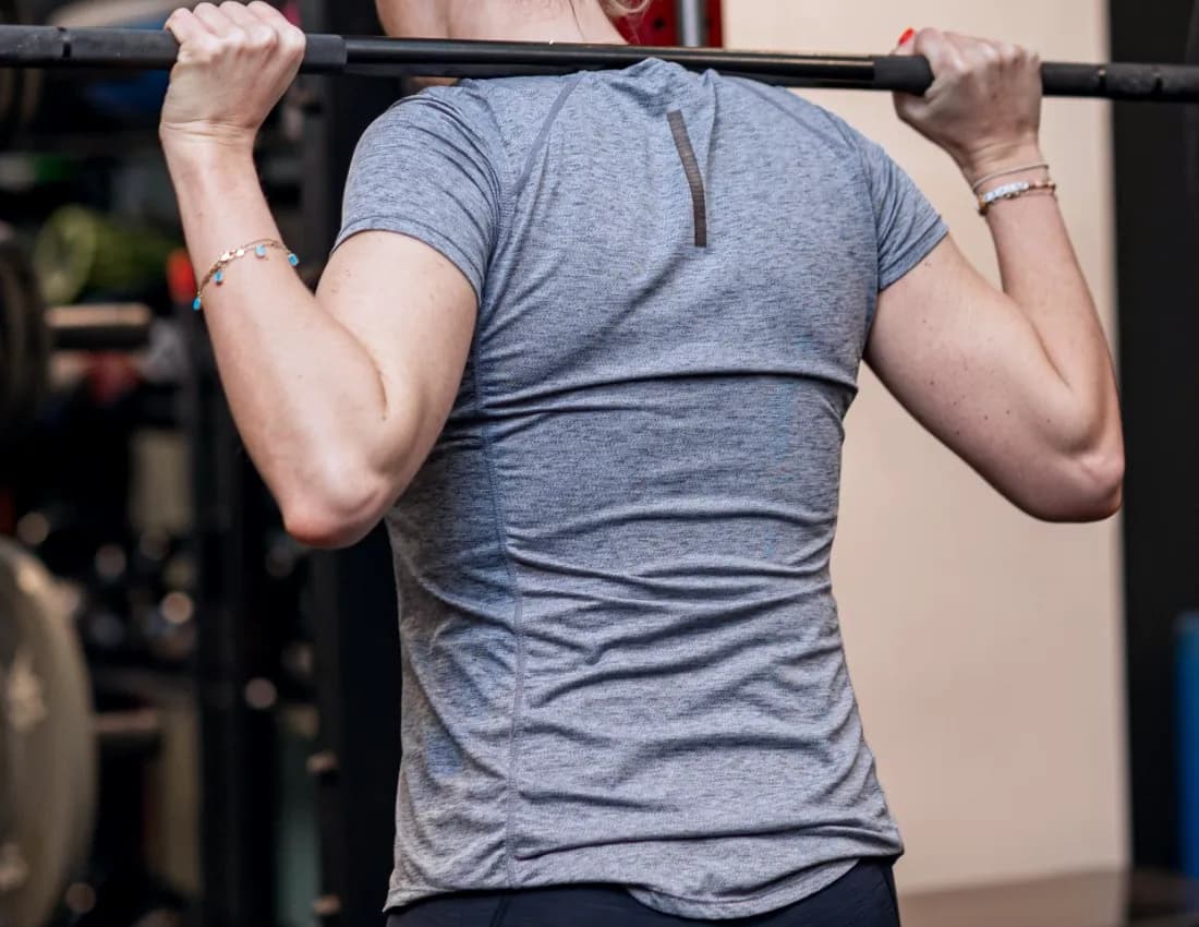 The back of a woman holding a barbell across her shoulders