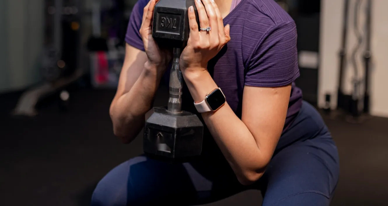 Close-up of a woman in a squat holding a dumbbell at her chest with both hands